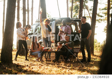 Near the car that is parked behind them. Group of friends are having fun together in the forest 131364910