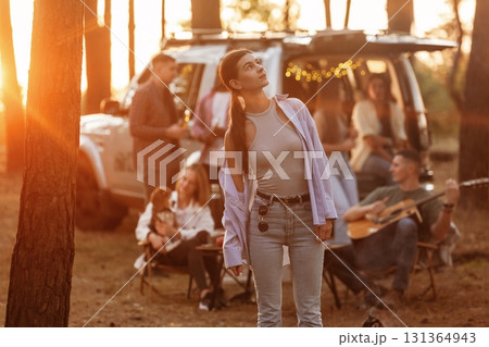 Girl in casual clothes is standing and posing. Group of friends are having fun together in the forest Girl in casual clothes is standing and posing. Group of friends are having fun together in the forest 131364943