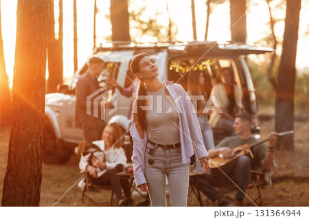 Girl in casual clothes is standing and posing. Group of friends are having fun together in the forest Girl in casual clothes is standing and posing. Group of friends are having fun together in the forest 131364944