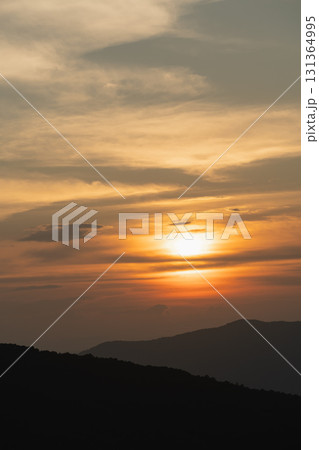 Serene Sunset Over Mountain Silhouette with Warm Hues and Soft Clouds Illuminating the Evening Sky in a Peaceful Natural Landscape 131364995