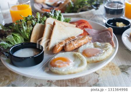 Breakfast Plate with Eggs, Ham, Sausages, Toast, Fresh Vegetables and Juice on a Table for a Delicious Morning Meal 131364998