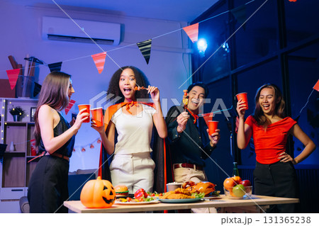 Joyful friends in vibrant Halloween costumes share drinks and laughter at a festive indoor party. 131365238