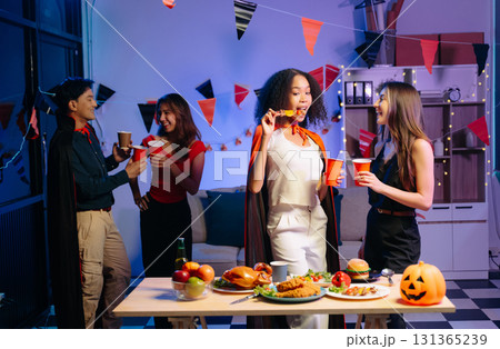 Joyful friends in vibrant Halloween costumes share drinks and laughter at a festive indoor party. 131365239