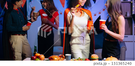 Joyful friends in vibrant Halloween costumes share drinks and laughter at a festive indoor party. 131365240