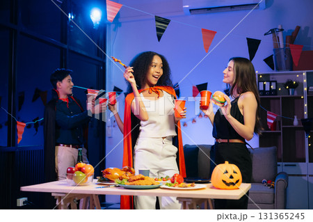 Joyful friends in vibrant Halloween costumes share drinks and laughter at a festive indoor party. 131365245