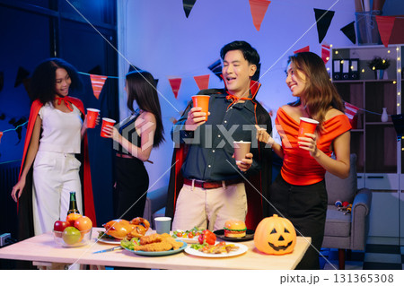 Joyful friends in vibrant Halloween costumes share drinks and laughter at a festive indoor party. 131365308