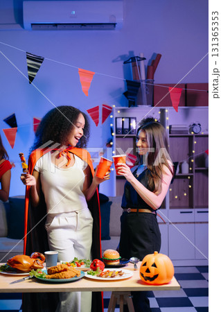 Joyful friends in vibrant Halloween costumes share drinks and laughter at a festive indoor party. 131365353