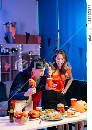 Joyful friends in vibrant Halloween costumes share drinks and laughter at a festive indoor party. 131365375