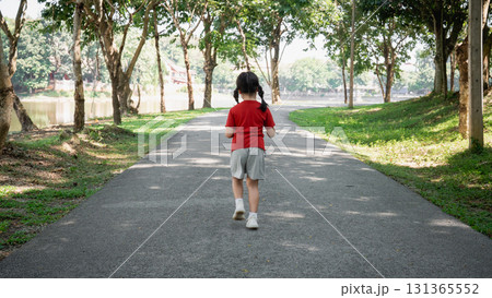 Young child walking alone on a peaceful pathway surrounded by trees in a serene park setting enjoying nature and fresh air on a sunny day Young child walking alone on a peaceful pathway surrounded by trees in a serene park setting enjoying nature and fresh air on a sunny day 131365552