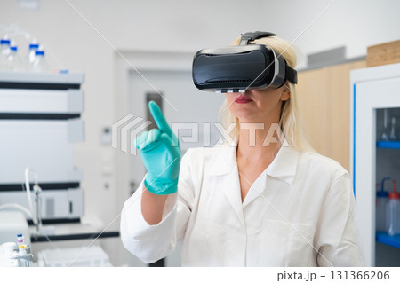 Female researcher wearing VR headset in a high tech chemical lab, performing virtual experiment simulation. Concept of augmented reality in science, digital data visualization, and innovative research 131366206