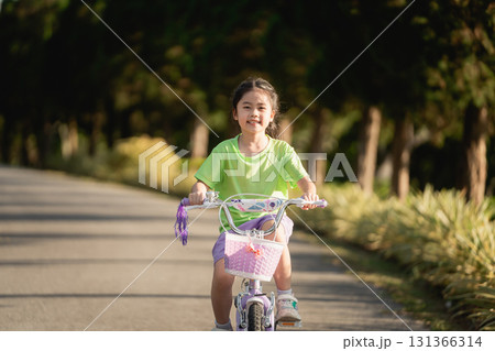 Young girl riding a bicycle on a sunny day in a peaceful park, enjoying outdoor activity and the joy of childhood in a vibrant natural setting 131366314