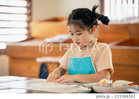 Young girl focused on baking and preparing dough in a bright kitchen, engaging in hands-on learning and developing culinary skills with love and joy 131366361