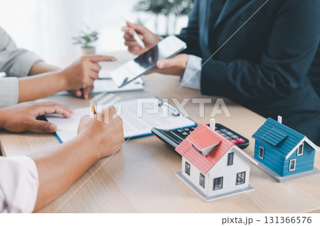 House model on desk with blurred people discussing contract in background, concept of real estate investment, mortgage loan, home ownership, property business and financial agreement. 131366576