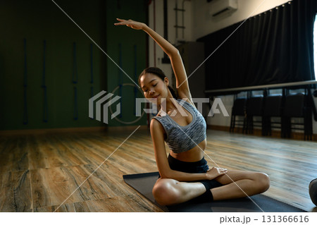 Calm female athlete practicing side stretch pose during yoga session in a modern fitness studio Calm female athlete practicing side stretch pose during yoga session in a modern fitness studio 131366616