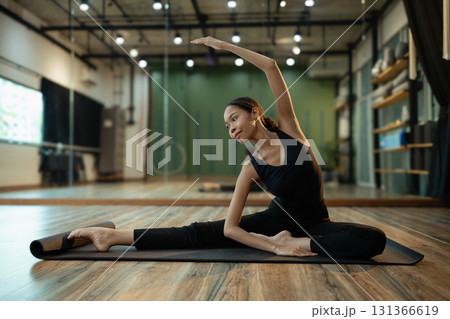 Calm female athlete practicing side stretch pose during yoga session in a modern fitness studio Calm female athlete practicing side stretch pose during yoga session in a modern fitness studio 131366619