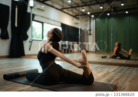 Female yogi in black outfit doing a backbend stretch pose in a spacious studio Female yogi in black outfit doing a backbend stretch pose in a spacious studio 131366620