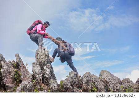 Two hikers on rocky mountain peak helping each other climb, symbol of teamwork, leadership, support, adventure, success, trust, exploration and outdoor lifestyle motivation in nature. Two hikers on rocky mountain peak helping each other climb, symbol of teamwork, leadership, support, adventure, success, trust, exploration and outdoor lifestyle motivation in nature. 131366627