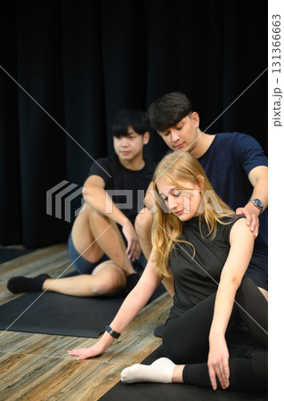 Trainer helping woman perform spinal twist yoga stretch on mat Trainer helping woman perform spinal twist yoga stretch on mat 131366663