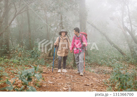 Two hikers walking together on forest trail in foggy weather with backpacks and trekking poles, symbol of adventure, teamwork, outdoor lifestyle, exploration, journey and travel inspiration. Two hikers walking together on forest trail in foggy weather with backpacks and trekking poles, symbol of adventure, teamwork, outdoor lifestyle, exploration, journey and travel inspiration. 131366700