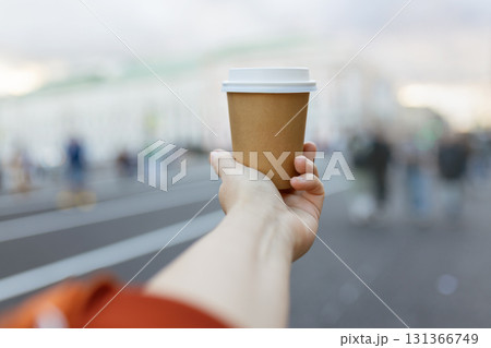 Brown paper cup of drink in women's hand on city street 131366749
