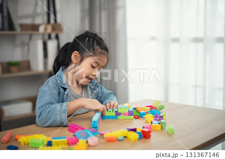 Young Girl Engaged in Creative Play with Colorful Building Blocks at Home in Natural Light, Focused on Developing Skills and Imagination Young Girl Engaged in Creative Play with Colorful Building Blocks at Home in Natural Light, Focused on Developing Skills and Imagination 131367146