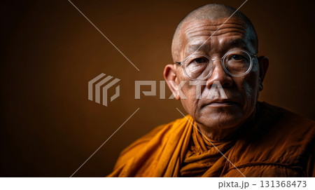 Bald elderly Asian monk wearing orange robe and round eyeglasses, calm expression, studio lighting, brown background 131368473