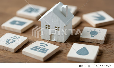 Wooden house model surrounded by wooden tiles with energy and water icons on wooden surface, symbolizing sustainable home concepts 131368697