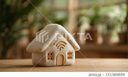 Soft fabric house model with wifi symbol on wooden table in cozy indoor setting with blurred plants in background 131368699