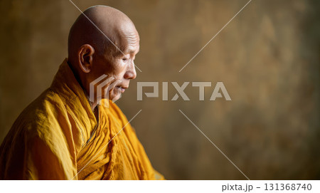 Elderly monk in yellow robe meditates peacefully with closed eyes against blurred brown background, expressing calm and wisdom Elderly monk in yellow robe meditates peacefully with closed eyes against blurred brown background, expressing calm and wisdom 131368740