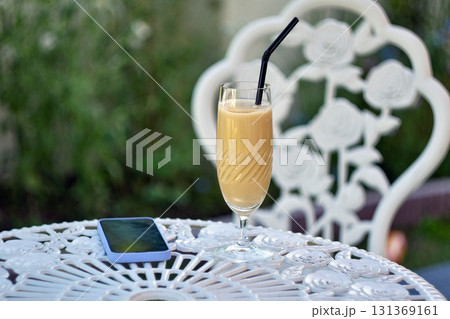 Iced latte with straw on outdoor white table 131369161