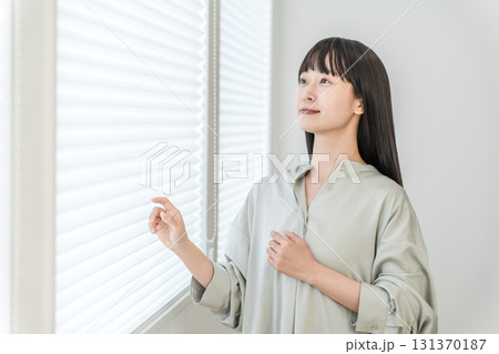 リビングの窓辺に立つ若いアジア人女性（プリーツスクリーン,ハニカムシェード） 131370187