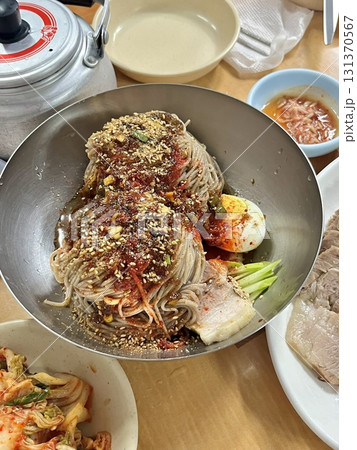 Naengmyeon, a refreshing Korean cold noodle dish served in an icy broth, topped with sliced vegetables, a boiled egg, and spicy sauce. Perfect for summer food photography and Korean cuisine projects. 131370567