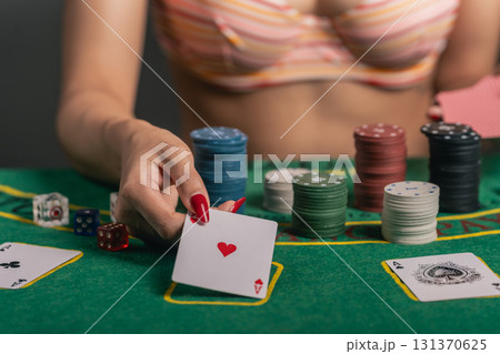 Close-up of a Sexy Woman in a Bra Playing Poker, Holding a Playing Card with Heart Symbol on a Green Felt Table Surrounded by Colorful Chips and Dice Close-up of a Sexy Woman in a Bra Playing Poker, Holding a Playing Card with Heart Symbol on a Green Felt Table Surrounded by Colorful Chips and Dice 131370625