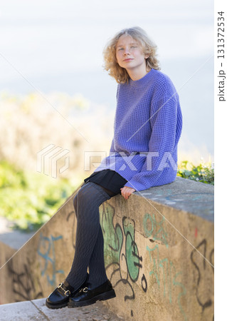 Young person sitting on concrete wall wearing casual clothes Young person sitting on concrete wall wearing casual clothes 131372534