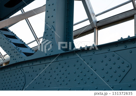 Close up of industrial steel bridge construction, blue painted structure with rivets and beams, modern architecture, geometric details and clear sky in the background Close up of industrial steel bridge construction, blue painted structure with rivets and beams, modern architecture, geometric details and clear sky in the background 131372635