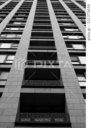 Black and white view of modern skyscraper with decorative balcony railings, architectural details, geometric patterns, and glass windows, shot from the ground up 131372639