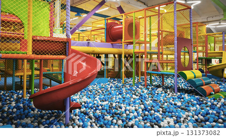 Colorful indoor playground with slides, climbing structures, and a ball pit full of blue, white, and black plastic balls, perfect for kids fun and birthday parties.  131373082