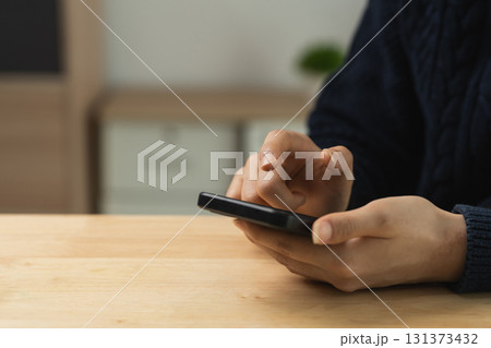 Person Using Smartphone at a Wooden Table, Focusing on Mobile Device with Hands in a Casual Indoor Environment 131373432