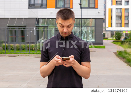 man holds smartphone in modern urban area during daytime near contemporary buildings. White caucasian young man uses smart phone for checking latest news, surfs sites. Businessperson surfing Internet man holds smartphone in modern urban area during daytime near contemporary buildings. White caucasian young man uses smart phone for checking latest news, surfs sites. Businessperson surfing Internet 131374165