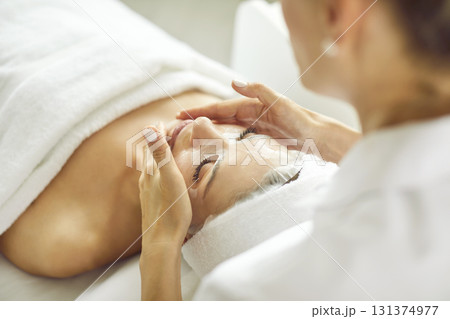 Cosmetologist at beauty and spa salon applies sheet mask on face of relaxed young woman 131374977