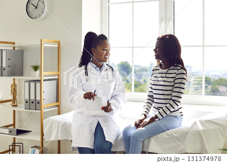 Happy African American female doctor and patient talking in examination room at clinic Happy African American female doctor and patient talking in examination room at clinic 131374978