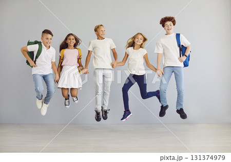 Happy school children looking cheerful at camera, holding hands and jumping together. Happy school children looking cheerful at camera, holding hands and jumping together. 131374979