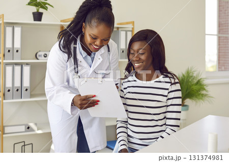 Happy young African American female doctor and patient looking at clipboard together 131374981