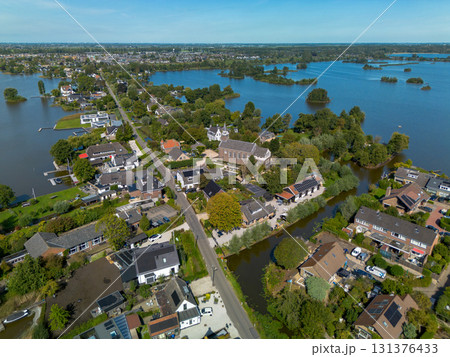 Aerial view of a small town with a central church and tall steeple, surrounded by houses, tree lined streets, and nearby lakes with islands, blending historic charm and natural beauty. Aerial view of a small town with a central church and tall steeple, surrounded by houses, tree lined streets, and nearby lakes with islands, blending historic charm and natural beauty. 131376433