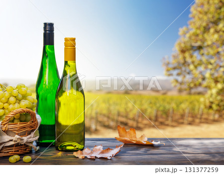 Wine bottles with grapes on a wooden table, glowing with sunny vineyard bokeh in the background 131377259