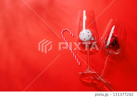 Wine glasses with Christmas baubles inside on red background, mockup for holiday card or invitation Wine glasses with Christmas baubles inside on red background, mockup for holiday card or invitation 131377282