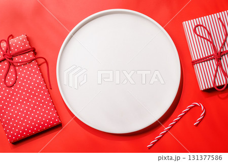 Empty plate with snowy fir branches and gift boxes on red background, Christmas food mockup 131377586