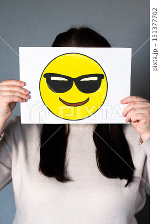 Woman holding happy emoji with sunglasses mask in front of face. Social media trends, Gen Z marketing, World emoji day 17 July. Woman holding happy emoji with sunglasses mask in front of face. Social media trends, Gen Z marketing, World emoji day 17 July. 131377702
