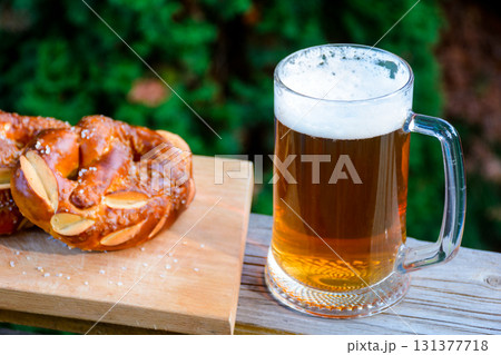 having beer and pretzel outdoors. celebrate oktoberfest. glass mug with cold beverage on the dark background of garden. rustic scene having beer and pretzel outdoors. celebrate oktoberfest. glass mug with cold beverage on the dark background of garden. rustic scene 131377718