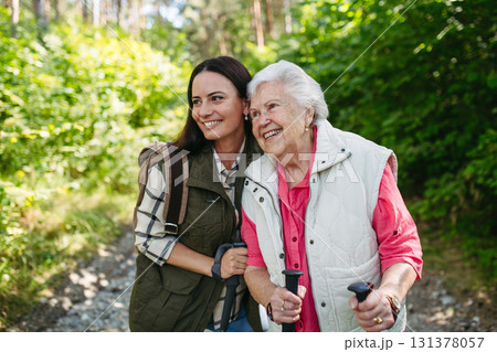 Senior woman and daughter enjoying hike with trekking poles. 131378057